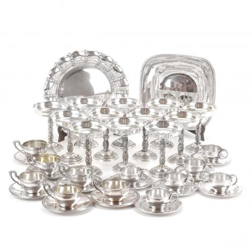 Hallmarked centerpieces, one marked A. Pallé., two cup sets with their plates, one hallmarked by Armengol; twelve glasses with Barcelona hallmark.Centerpieces, 23 cm. diam. and 26 cms. diam. Glasses 13 cms. high.1480 gr. Centerpieces and cups with plates. 1734 gr. Glasses with counterweight.  